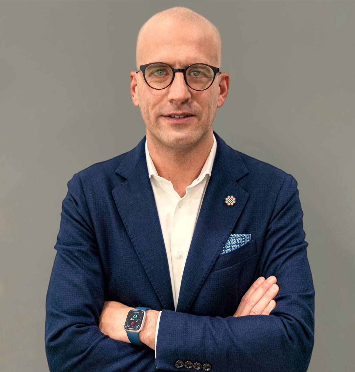 Foto di Carlo Apostoli a mezzo busto con braccia incrociate, camicia bianca, giacca blu su sfondo grigio